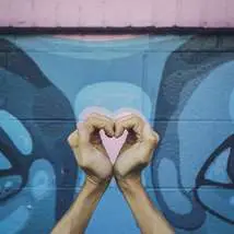 Man cupping hands into loveheart in front of graffiti by marcel free to use from unsplash
